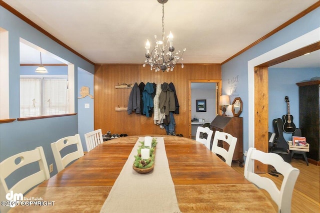 dining space featuring wooden walls, a notable chandelier, wood finished floors, and ornamental molding