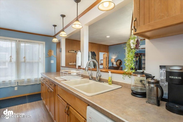 kitchen featuring decorative light fixtures, light countertops, ornamental molding, wood finished floors, and a sink