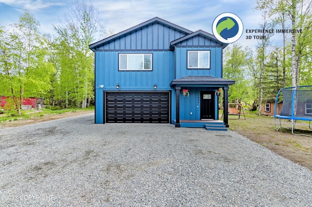 view of front facade with gravel driveway, an attached garage, a trampoline, and board and batten siding