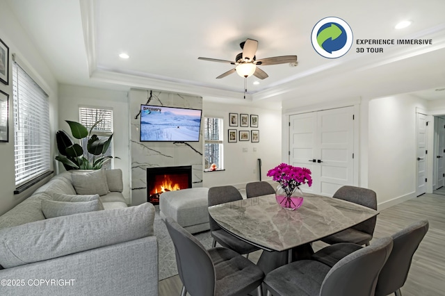 dining space featuring recessed lighting, a raised ceiling, a premium fireplace, light wood-style floors, and baseboards