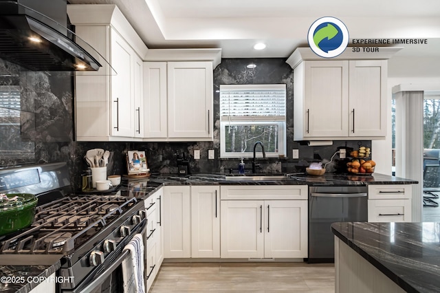 kitchen with stainless steel appliances, a sink, backsplash, dark stone counters, and wall chimney exhaust hood