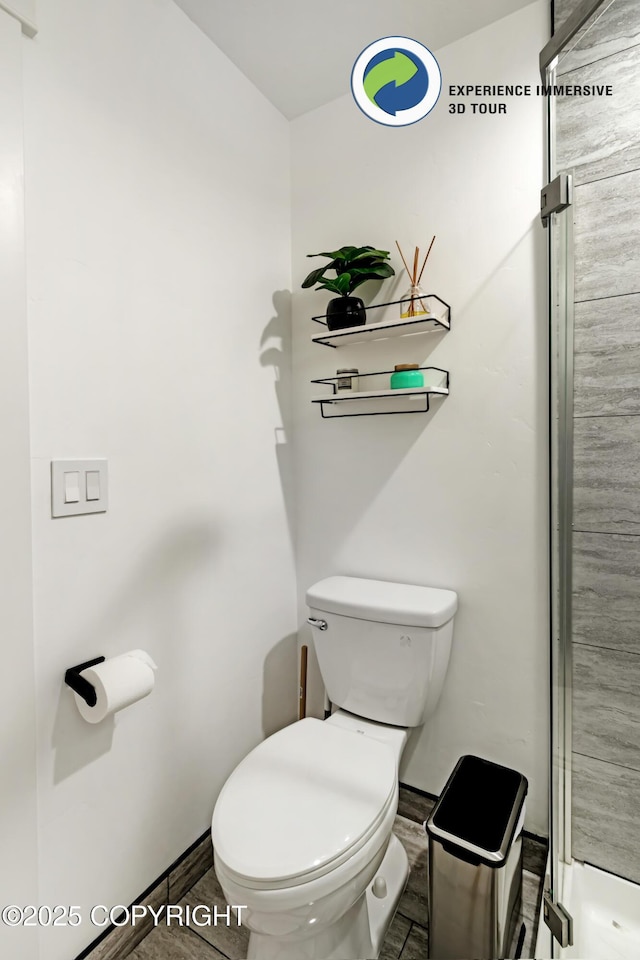 bathroom featuring toilet, a shower stall, and baseboards