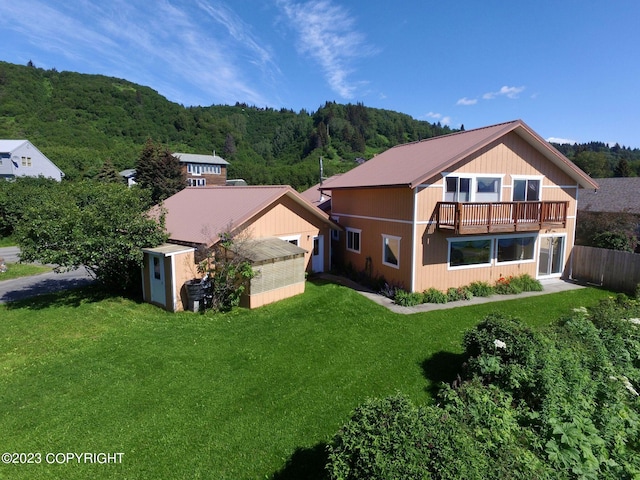 back of property with a balcony, an outdoor structure, and a lawn