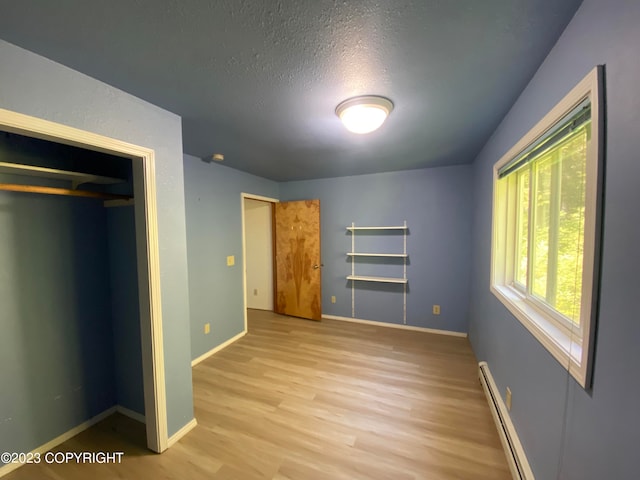 unfurnished bedroom with baseboard heating, a textured ceiling, a closet, and light hardwood / wood-style flooring