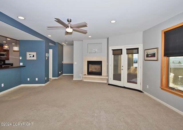 unfurnished living room featuring ceiling fan, carpet flooring, a tiled fireplace, and french doors