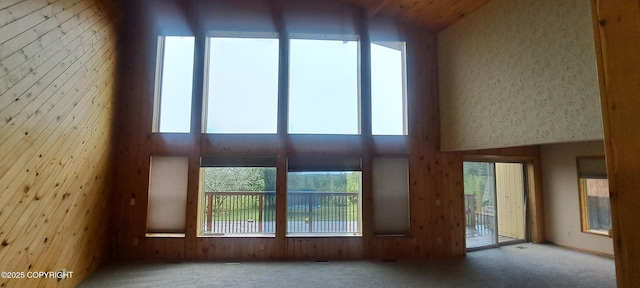 9450 Keshon Cir, Wasilla, AK 99654 - unfurnished living room featuring a towering ceiling, carpet flooring, healthy amount of natural light, and wood walls