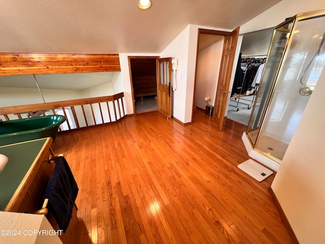 interior space featuring hardwood / wood-style flooring, lofted ceiling, a shower with door, and a textured ceiling