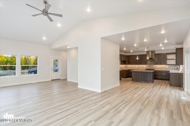 unfurnished living room featuring ceiling fan, light wood-type flooring, sink, and high vaulted ceiling