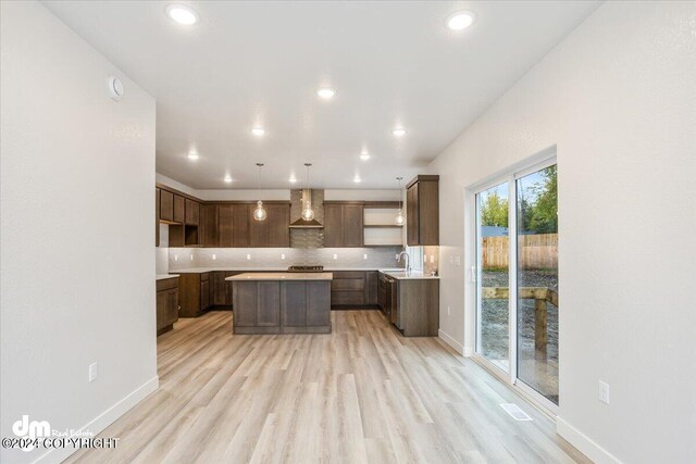 kitchen with wall chimney range hood, pendant lighting, light hardwood / wood-style flooring, sink, and a center island