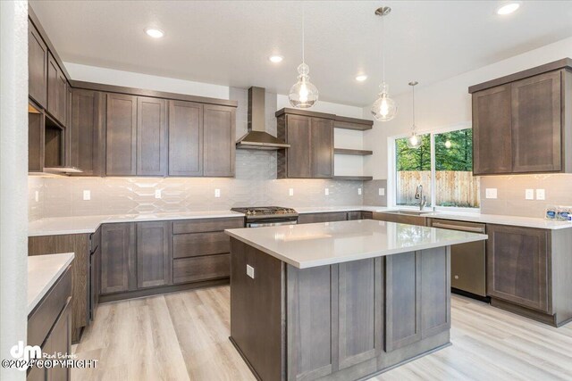 kitchen with a kitchen island, dark brown cabinets, wall chimney exhaust hood, stainless steel appliances, and light hardwood / wood-style floors