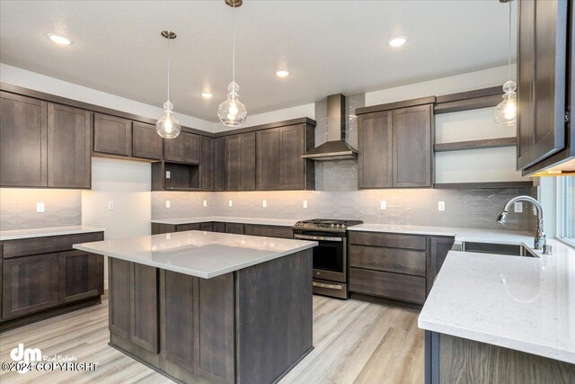 kitchen featuring wall chimney exhaust hood, stainless steel range, a kitchen island, light hardwood / wood-style flooring, and sink