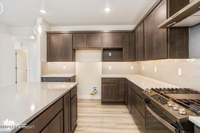 kitchen featuring light wood-type flooring, dark brown cabinetry, ventilation hood, hanging light fixtures, and stainless steel gas range oven