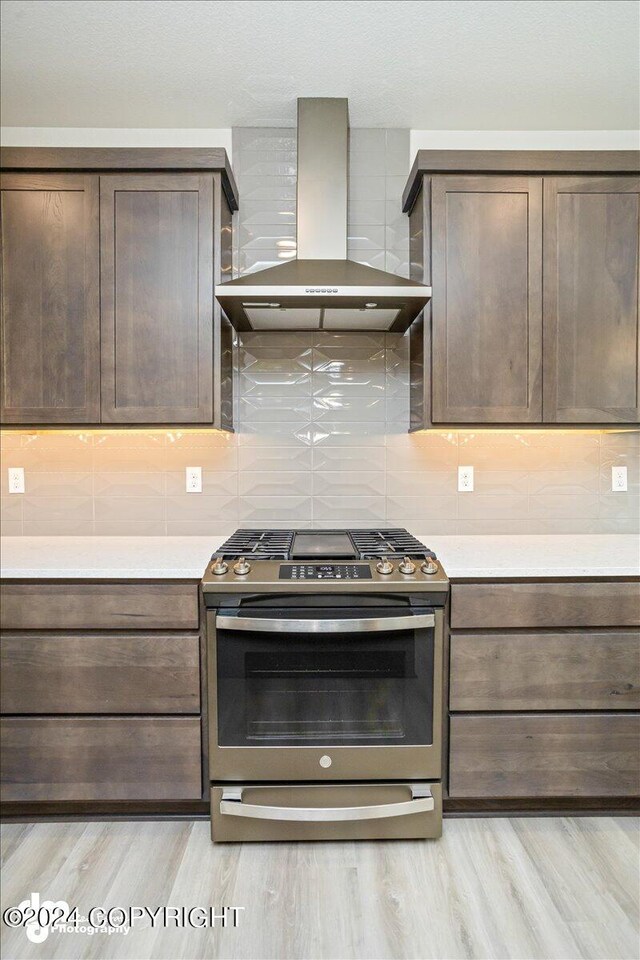 kitchen with wall chimney exhaust hood, stainless steel range, tasteful backsplash, and light hardwood / wood-style flooring