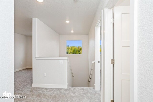 corridor featuring a textured ceiling and light colored carpet