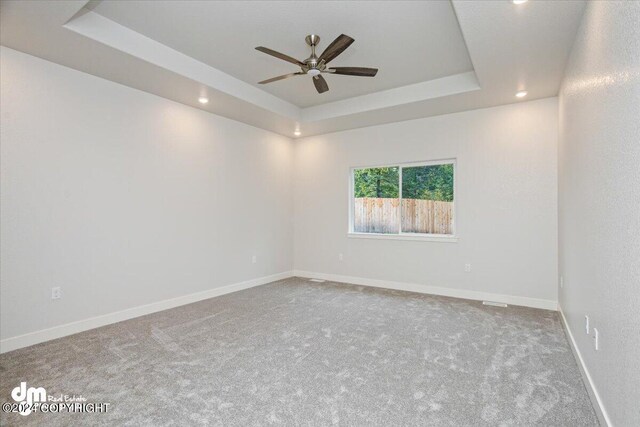 empty room featuring ceiling fan, a raised ceiling, and carpet