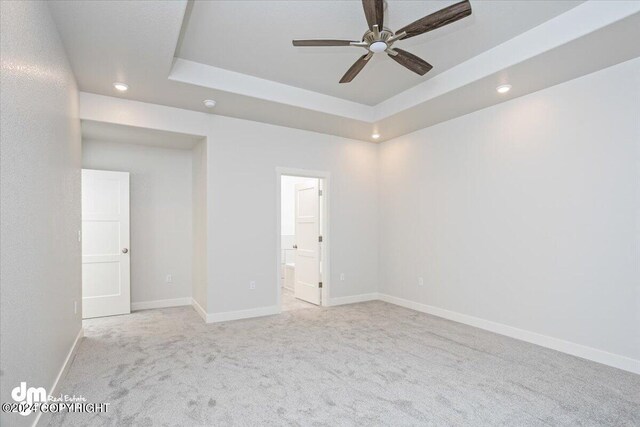 unfurnished room featuring light carpet, a tray ceiling, and ceiling fan