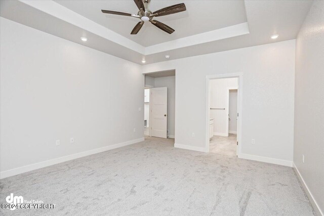 unfurnished bedroom with a raised ceiling, light colored carpet, ensuite bathroom, and ceiling fan