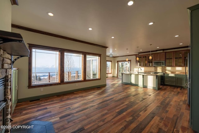 kitchen with a center island with sink, stainless steel appliances, light countertops, hanging light fixtures, and glass insert cabinets