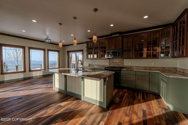 kitchen with a center island with sink, gas range, glass insert cabinets, stainless steel microwave, and hanging light fixtures