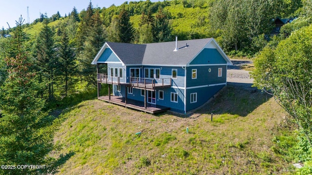 back of property with a deck, a view of trees, and a yard