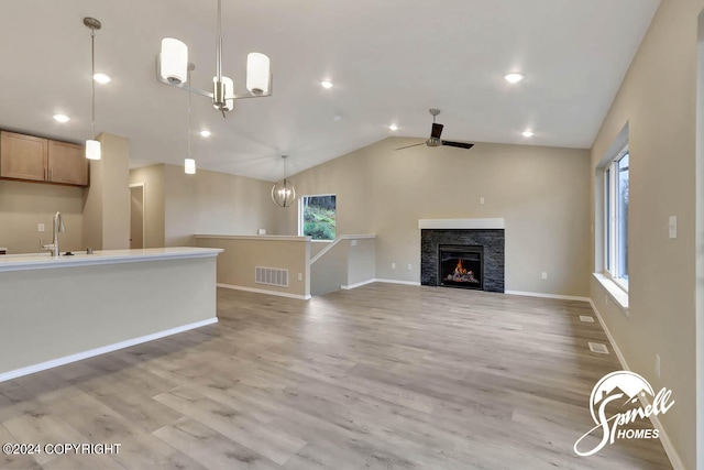 unfurnished living room featuring high vaulted ceiling, ceiling fan with notable chandelier, sink, and light wood-type flooring