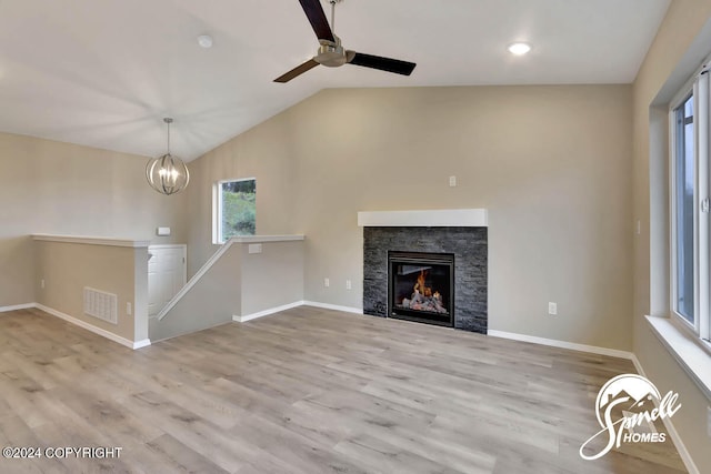 unfurnished living room featuring light hardwood / wood-style flooring, a stone fireplace, vaulted ceiling, and ceiling fan with notable chandelier