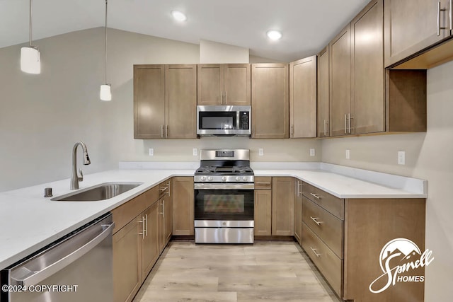 kitchen with pendant lighting, stainless steel appliances, light hardwood / wood-style floors, vaulted ceiling, and sink