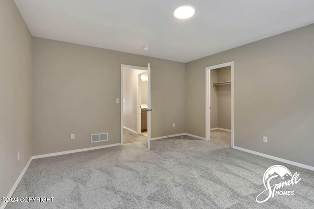 unfurnished bedroom featuring light carpet, a walk in closet, and a closet