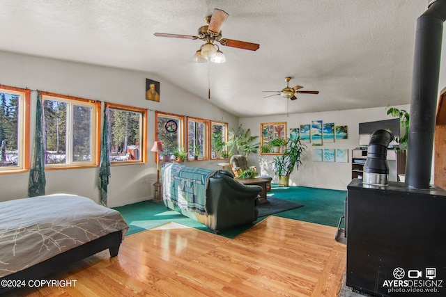 bedroom featuring ceiling fan, a textured ceiling, wood-type flooring, lofted ceiling, and a wood stove