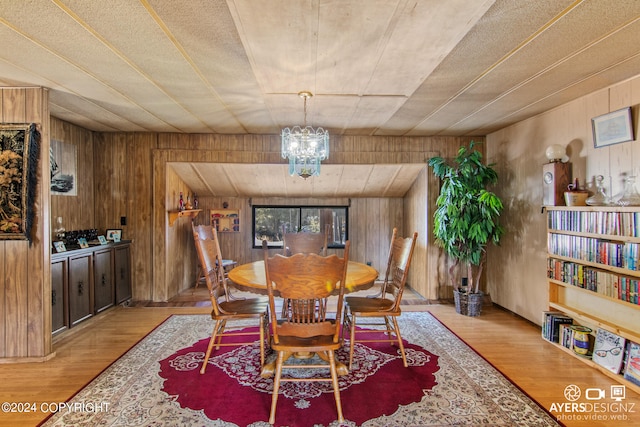 dining space featuring light hardwood / wood-style floors, wooden walls, and a chandelier