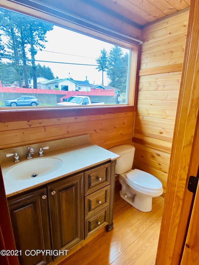 bathroom with wood walls, vanity, toilet, and wood-type flooring