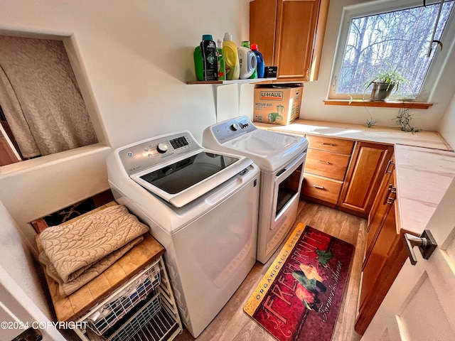 clothes washing area with light hardwood / wood-style floors, cabinets, and washer and clothes dryer