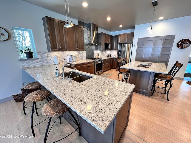 kitchen featuring appliances with stainless steel finishes, sink, wall chimney range hood, hanging light fixtures, and a kitchen breakfast bar