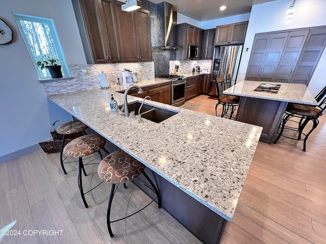 kitchen with appliances with stainless steel finishes, a breakfast bar area, light hardwood / wood-style floors, light stone counters, and sink