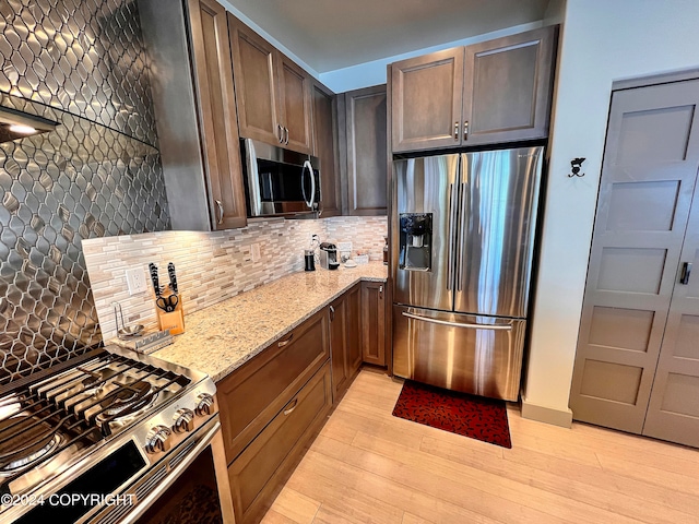 kitchen featuring light stone countertops, appliances with stainless steel finishes, tasteful backsplash, light hardwood / wood-style floors, and dark brown cabinetry