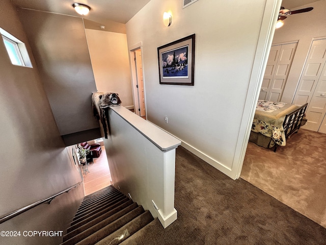 stairway with dark colored carpet and ceiling fan