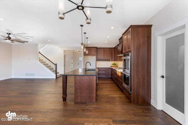 kitchen featuring pendant lighting, sink, dark hardwood / wood-style flooring, stainless steel double oven, and a center island with sink