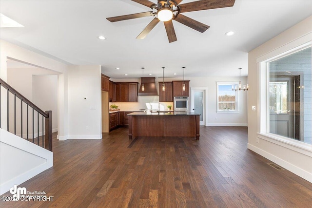 kitchen featuring dark hardwood / wood-style flooring, wall chimney range hood, decorative light fixtures, and a center island with sink