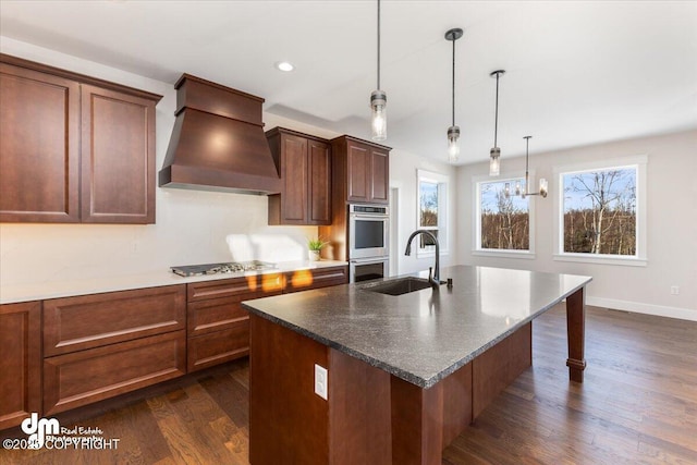 kitchen featuring sink, custom range hood, an island with sink, dark hardwood / wood-style flooring, and decorative light fixtures