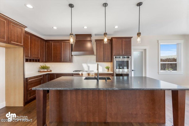 kitchen featuring sink, decorative light fixtures, a center island with sink, and premium range hood