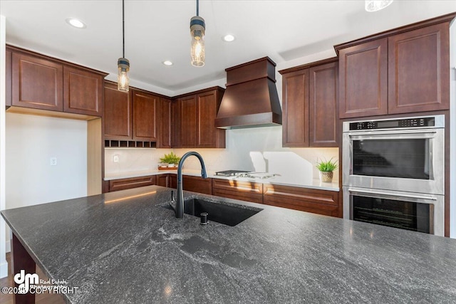 kitchen featuring sink, custom exhaust hood, a center island with sink, appliances with stainless steel finishes, and pendant lighting