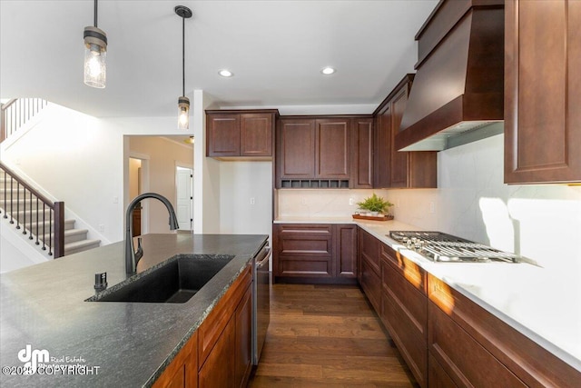 kitchen featuring dark wood-type flooring, sink, custom exhaust hood, stainless steel dishwasher, and pendant lighting