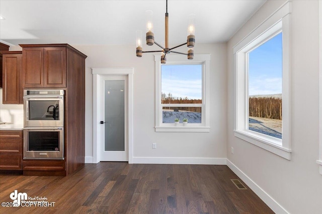 kitchen with stainless steel double oven, a healthy amount of sunlight, dark hardwood / wood-style flooring, and a notable chandelier