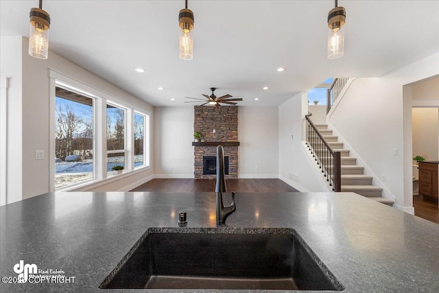 kitchen featuring pendant lighting, sink, a stone fireplace, and dark hardwood / wood-style flooring