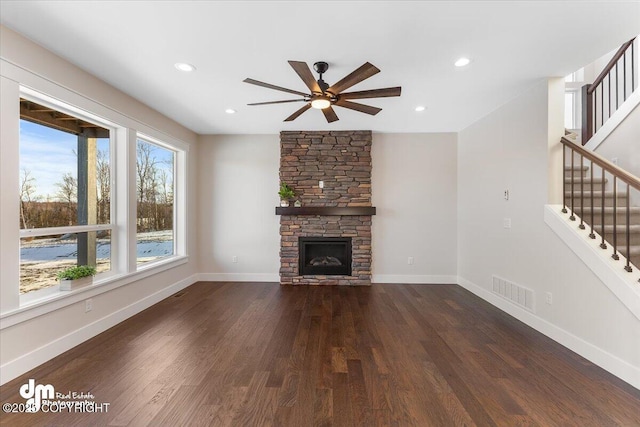 unfurnished living room featuring a stone fireplace, dark wood-type flooring, and ceiling fan