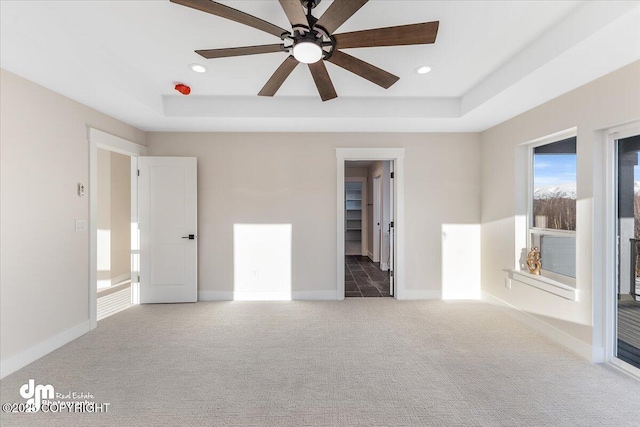 carpeted spare room with a tray ceiling and ceiling fan