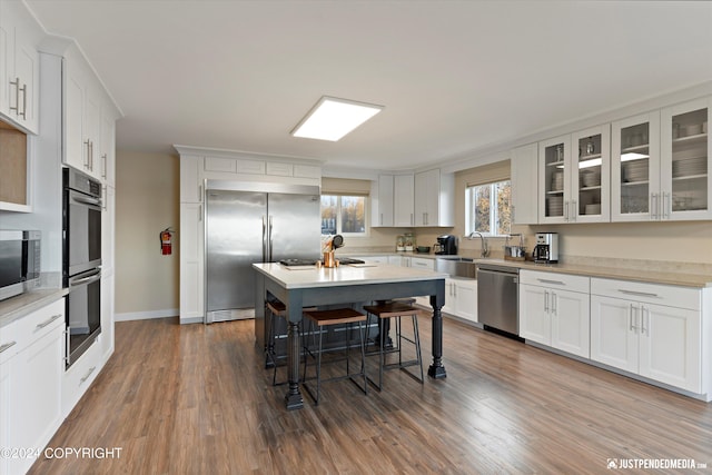 kitchen with appliances with stainless steel finishes, white cabinetry, wood-type flooring, and a kitchen island