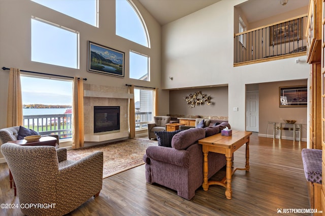 living room featuring a tiled fireplace, a water view, dark hardwood / wood-style flooring, and a high ceiling