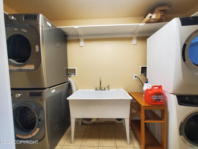 laundry room featuring stacked washer and clothes dryer, light tile patterned flooring, and sink