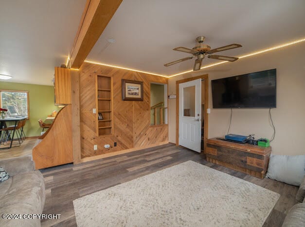 living room featuring wood walls, beamed ceiling, dark wood-type flooring, and ceiling fan